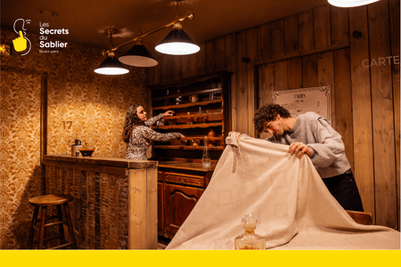 Deux joueurs participent à un escape game en duo dans la salle du Bar Clandestin des Secrets du Sablier à Strasbourg, résolvant des énigmes ensemble.